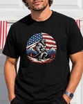 Bigfoot in front of American flag and mountains, wearing a t-shirt.