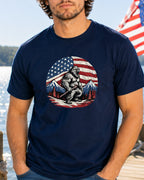 Bigfoot wearing a loincloth stands in front of an American flag and mountains.