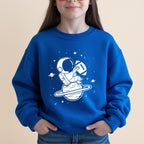 Child wearing blue sweatshirt with astronaut and football on planet design.