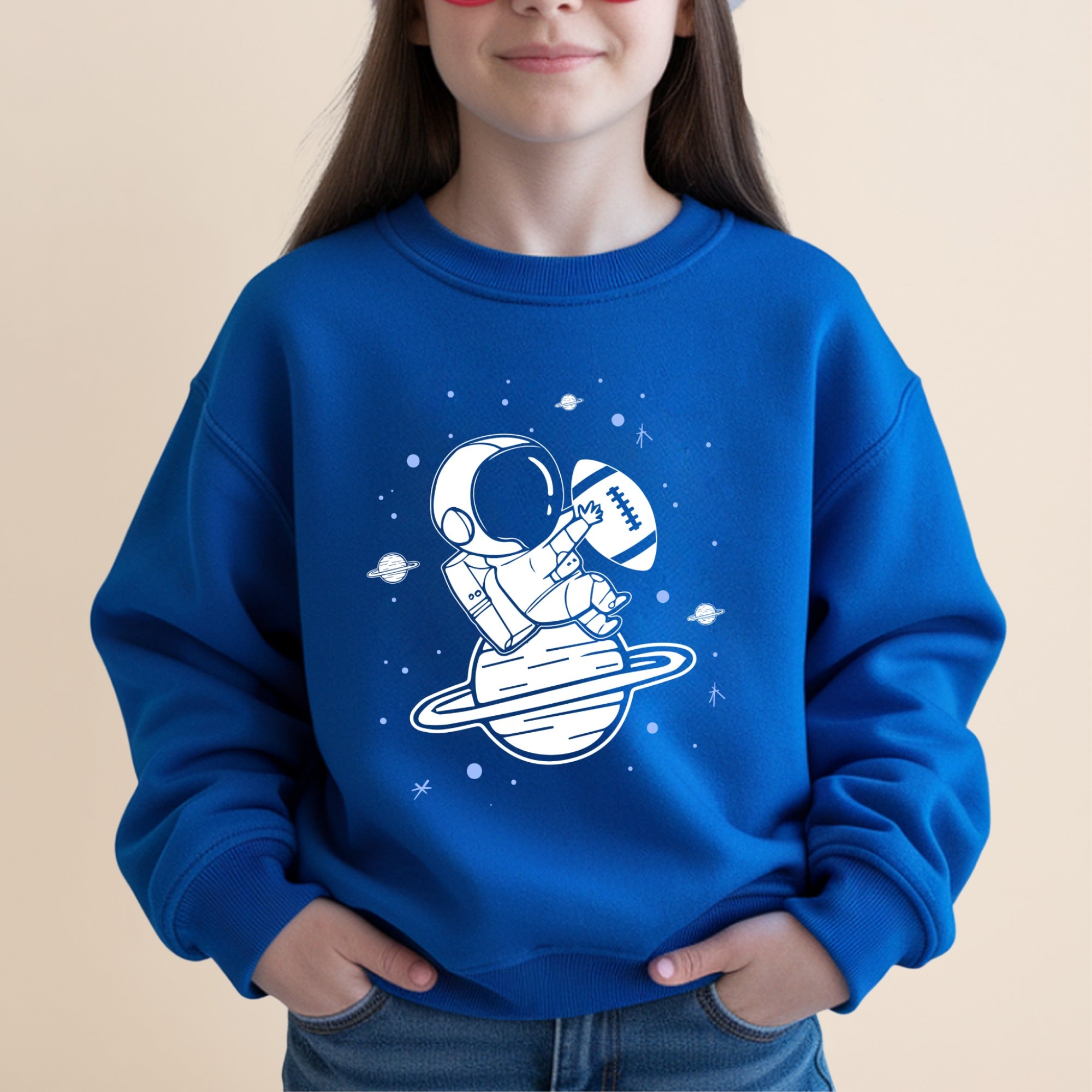Child wearing blue sweatshirt with astronaut and football on planet design.