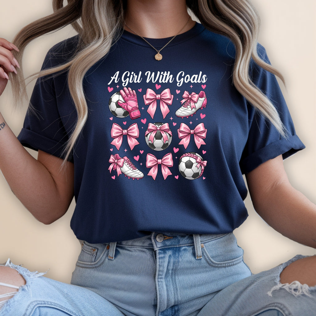 Navy t-shirt with pink soccer balls, cleats, and bows on a white background.
