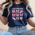 Navy t-shirt with pink soccer balls, cleats, and bows on a white background.