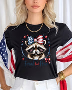 Black t-shirt with raccoon wearing patriotic bow, "Feral but Free" text.