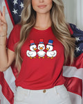 Three cartoon ducks in red, white, and blue hats on a red t-shirt.