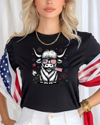 Highland cow with American flag sunglasses and fireworks graphic on black t-shirt.